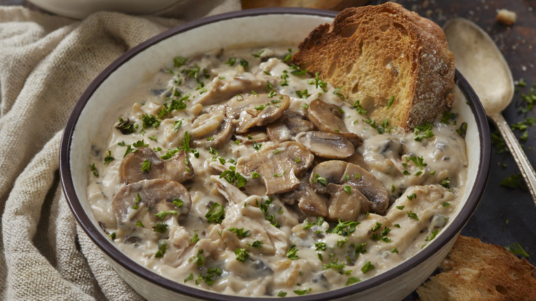 Cream of chicken soup in a white bowl with mushrooms and crusty bread. 