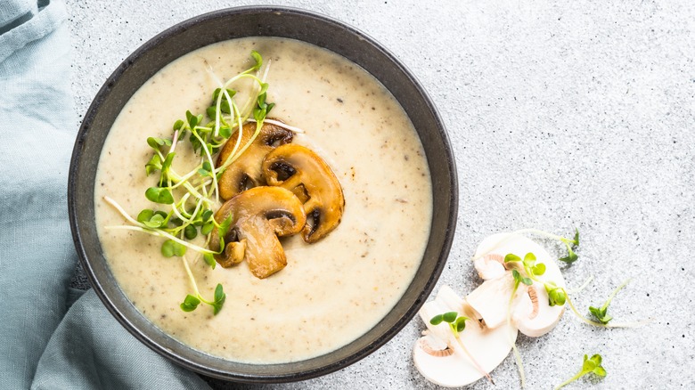 a bowl of cream of mushroom soup garnished with sprouts.