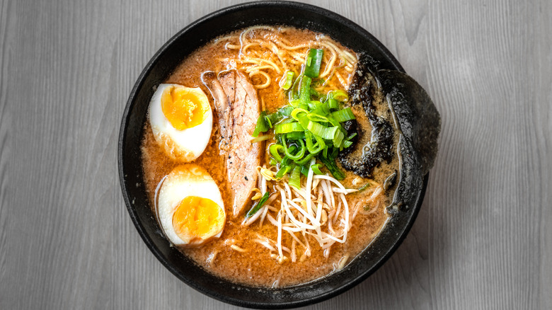 Ramen soup in a black bowl with chicken, egg and scallions.