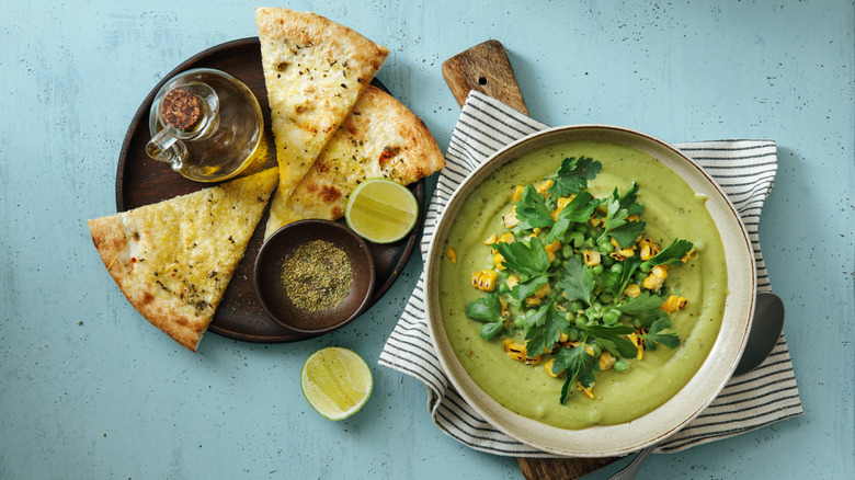 Split pea soup in a porcelain bowl with parsley, roasted corn and a side plate of pita bread. 