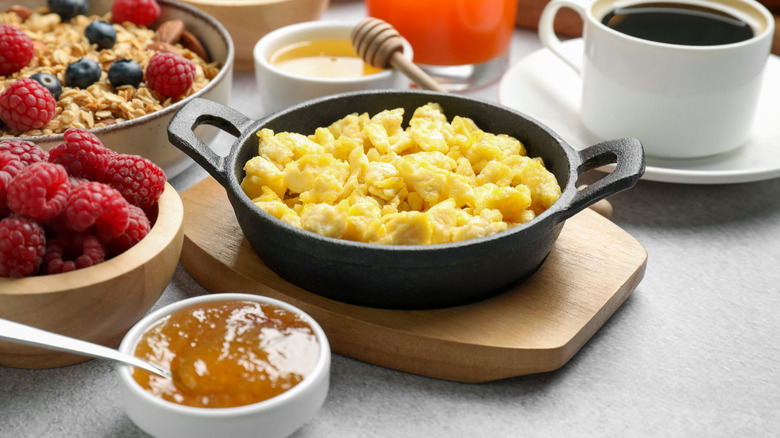 Scrambled eggs in a skillet next to granola, raspberries, honey, and coffee