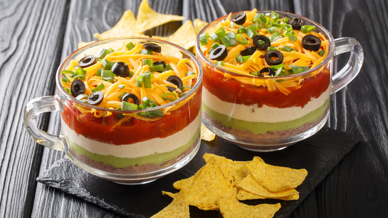 layered dip displayed in cups alongside tortilla chips