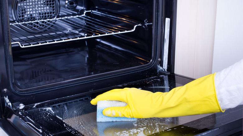 open oven with person cleaning it with yellow glove on