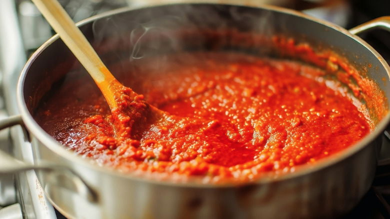 Tomato sauce simmering in a large pan with a wooden spoon resting on the edge