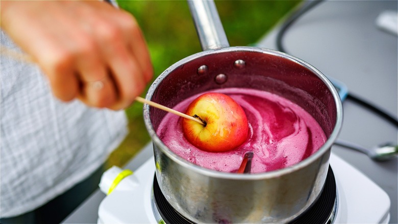 Hand dipping apple in candy coating