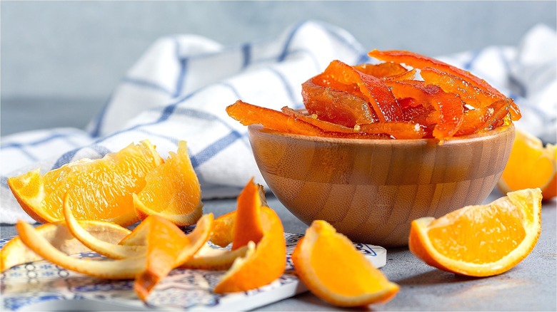 Candied citrus peels in wooden bowl surrounded by orange slices