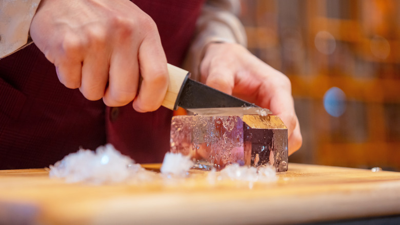 A man shaping a block of clear ice for ice cubes.