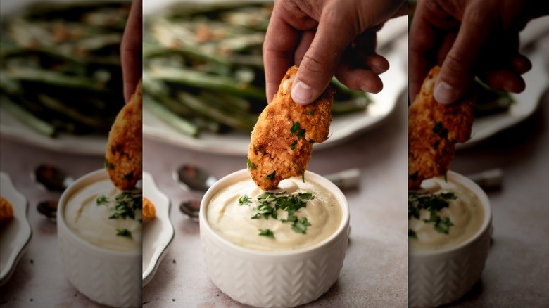 person dipping a chicken tender in creamy sauce