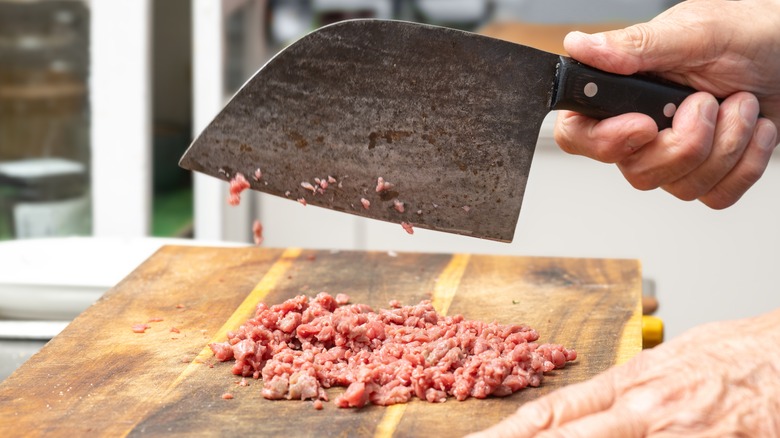 Cook mincing beef with cleaver on wooden board