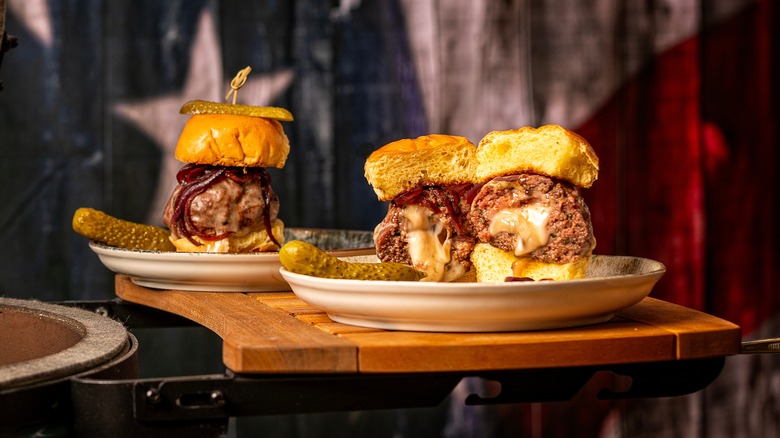 Three mozzarella-stuffed meatball sliders with pickles on the side in front of an American flag