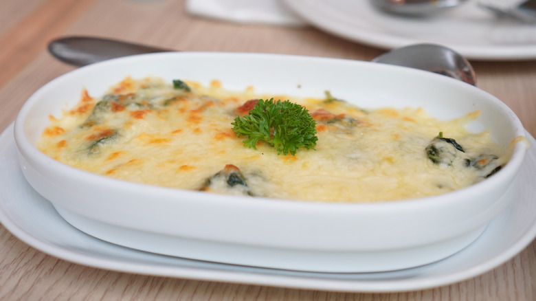 A ceramic dish of creamed spinach has a layer of melted cheese on top.