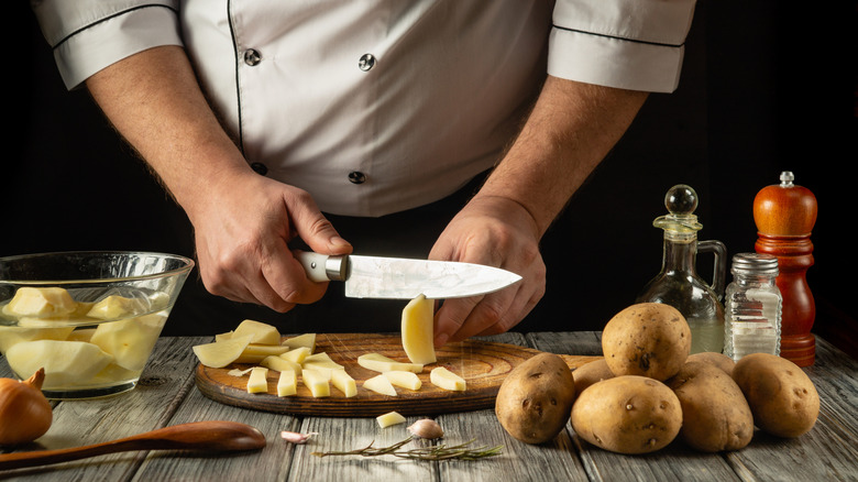 a chef slices raw potato, with more potato soaking in cold water next to them