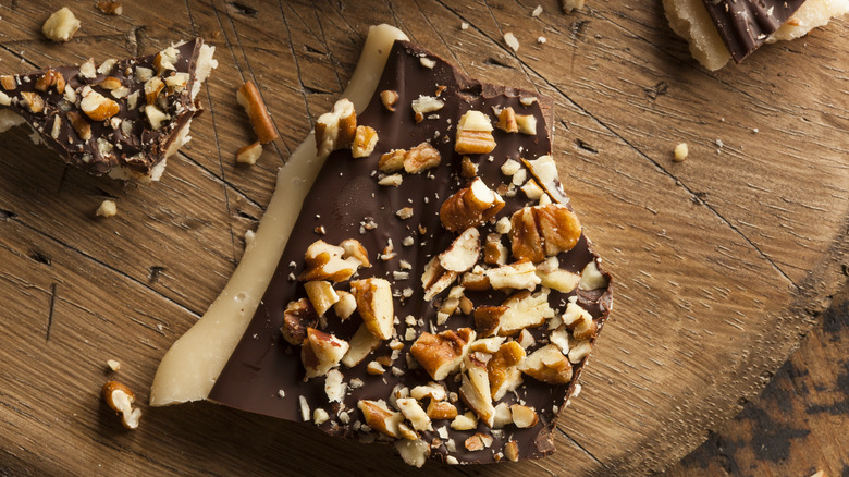 Slabs of toffee covered in chocolate and nuts rest on a wooden table