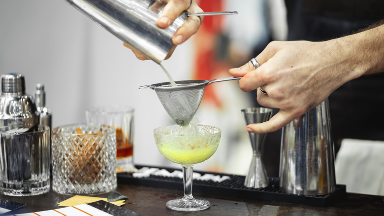 bartender straining cocktail into coupe