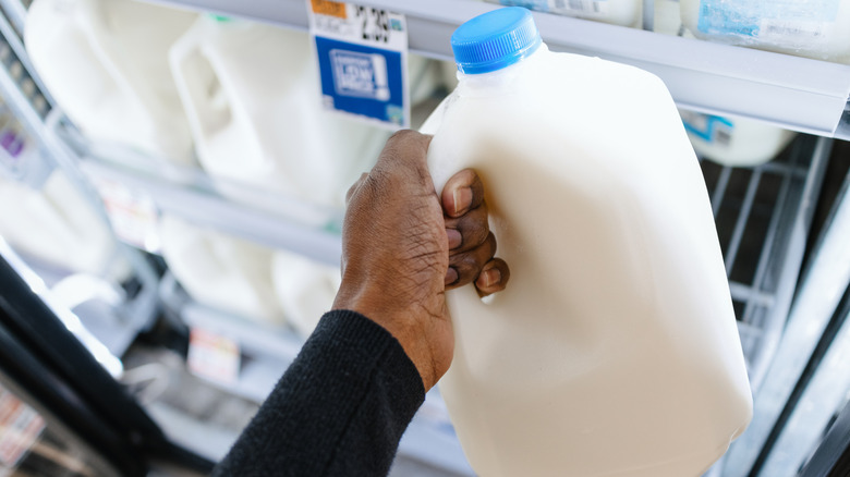 A hand grasps a gallon of milk in the milk aisle