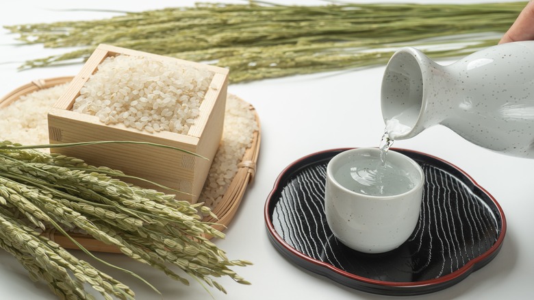 Sake being poured into cup beside box of rice