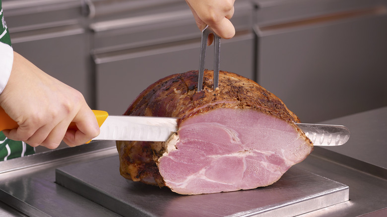 Ham being carved into slices with a sharp knife