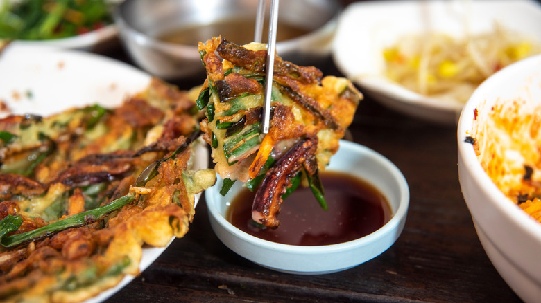 Person dipping green onion pancake into soy sauce