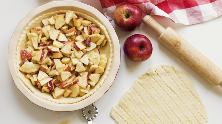 Applie pie filling in a bowl on a table with a rolling pin and crimped crust