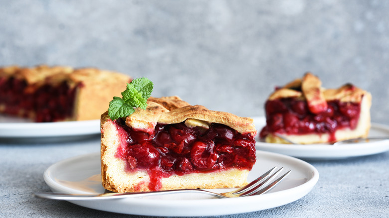 A slice of cherry pie sits on a plate, garnished with fresh mint