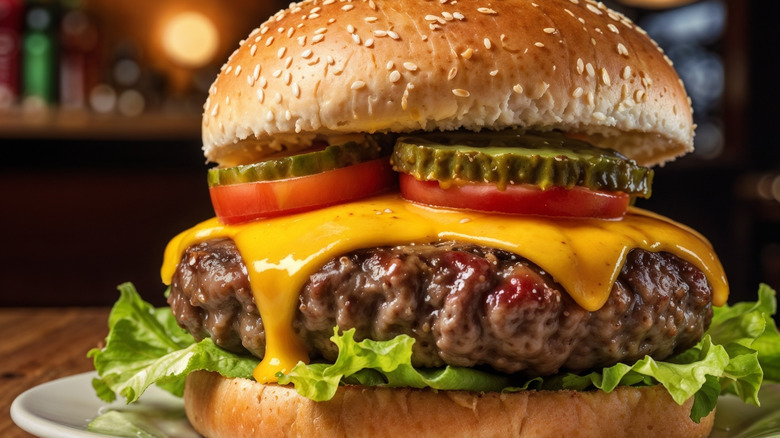 Closeup of a cheeseburger with a sesame seed bun, pickles, tomato, cheese, a thick patty, and lettuce