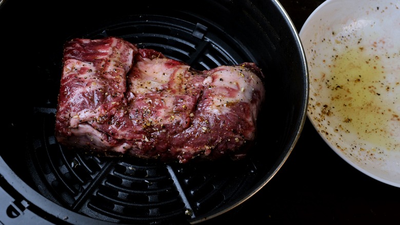 Small beef roast in an air fry basket with an oiled white dish next to it