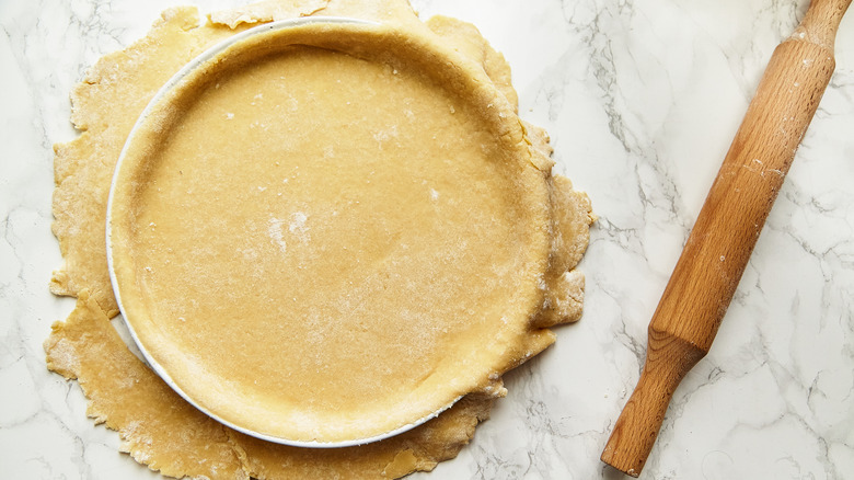 A pie crust next to a rolling pin