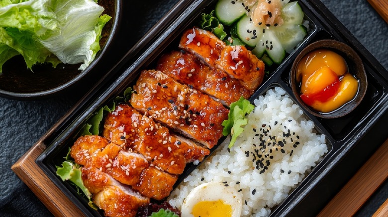 bento style black lunchbox with egg, rice, and glazed meat