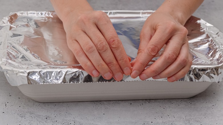 hands covering lasagna baking tray with aluminum foil