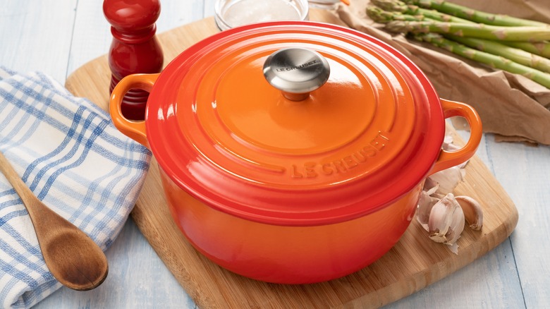 A Le Creuset dutch oven on a wooden cutting board.