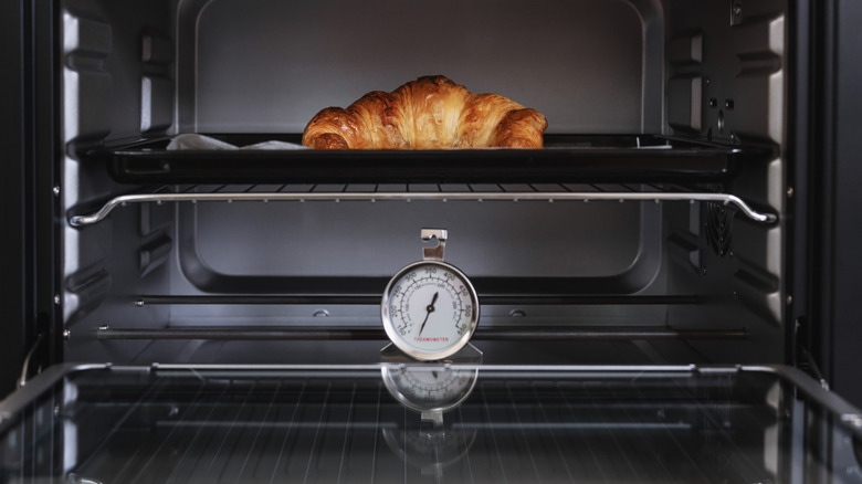 Oven thermometer and croissant in center of oven