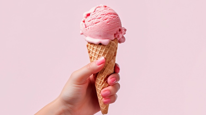 Hand holding a pink scoop of ice cream on a waffle cone