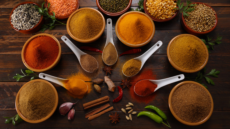 bowls and spoonfuls of spices on wood table