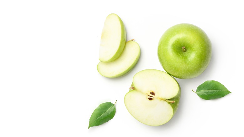 Whole, half, and slices of green apple with leaves