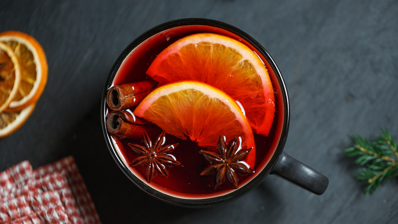 Glass of mulled wine with orange slices, star anise, and cinnamon sticks in black mug