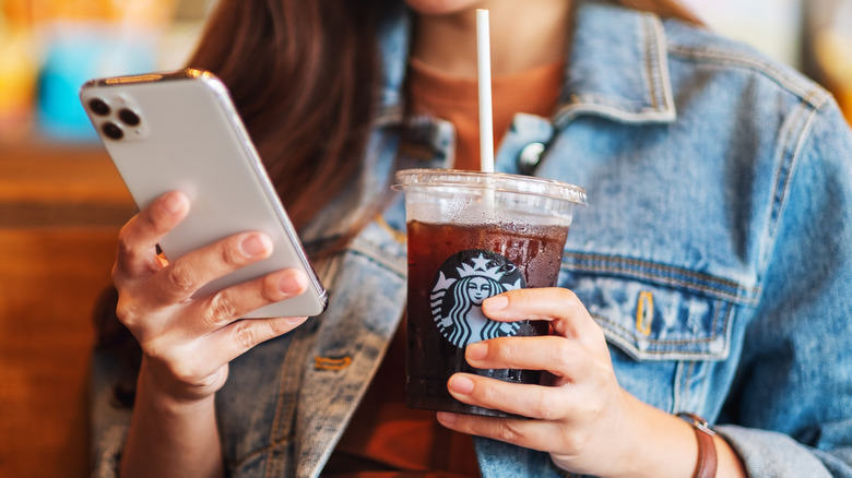 Woman holding iced Starbucks drink and using app on iPhone