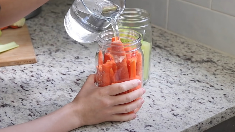 Pouring water over cut carrots in a jar