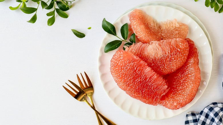 Grapefruit segments on a white place with a sprig of leaves and two forks on the side