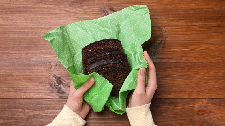 Hands wrapping sliced rye bread in green beeswax wrap