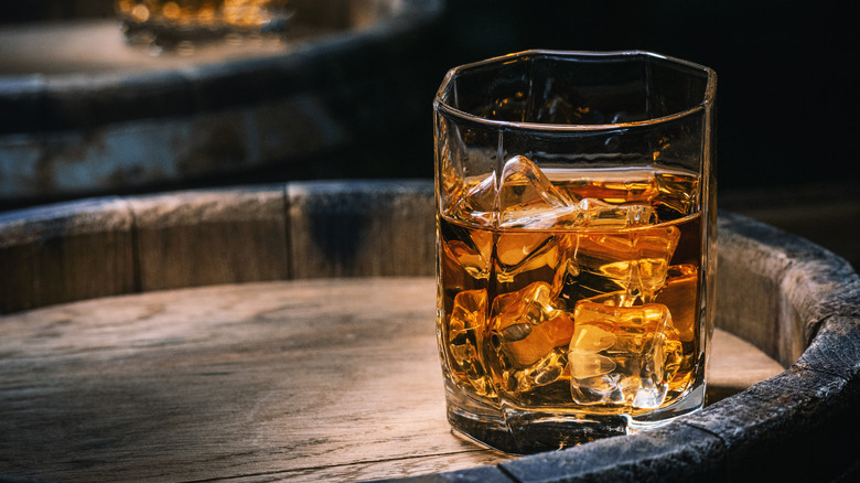 Glass of whiskey with ice on a barrel