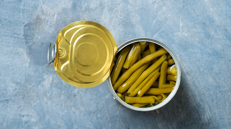 overhead shot of an opened can of green beans on a blue surface