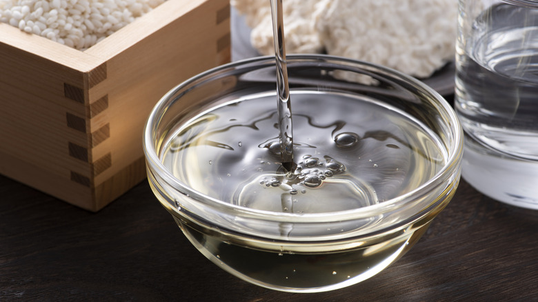 Mirin being poured into small glass bowl surrounded by rice