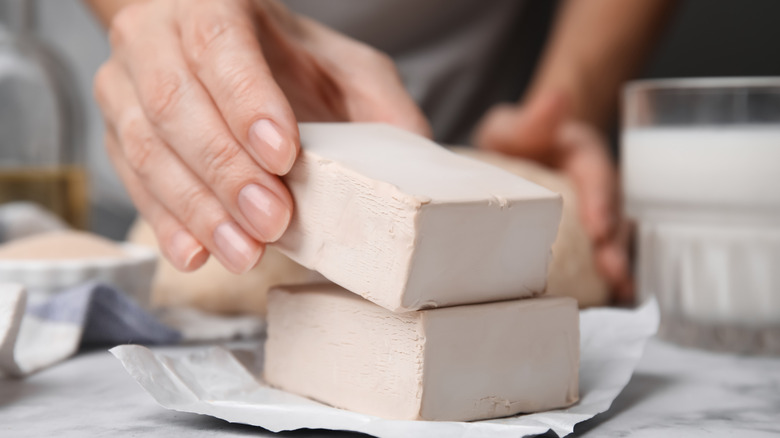 A hand handles a block of compressed yeast stacked on top of another atop a kitchen counter.