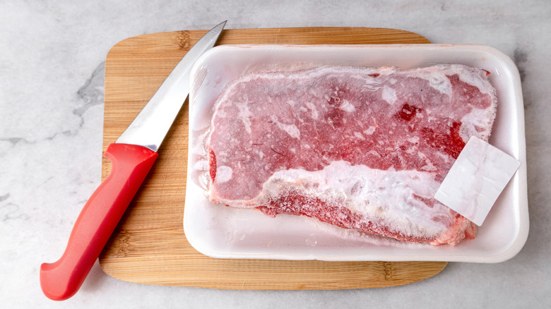 Package of frozen steak on cutting board