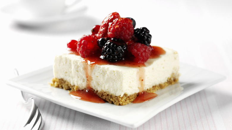 A square of no-bake cheese cake is topped wit berries and jam