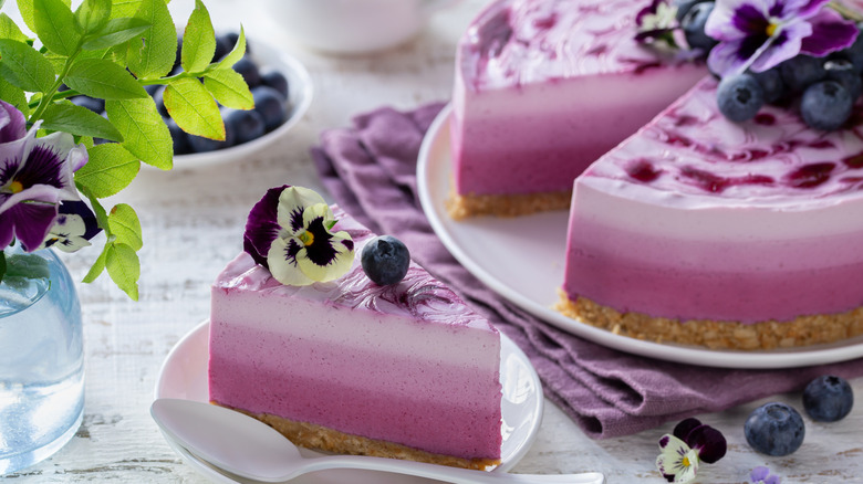 A no bake blueberry cheesecake has a slice removed and is topped with fresh berries and purple pansy flowers