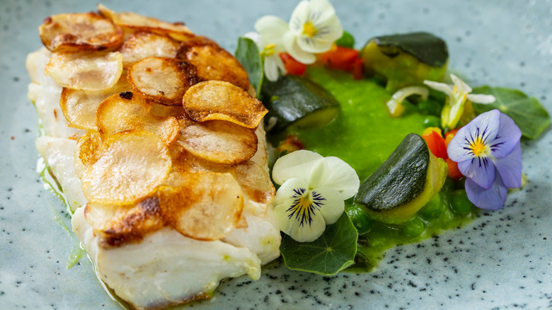 White fish topped with scalloped potatoes next to green sauce