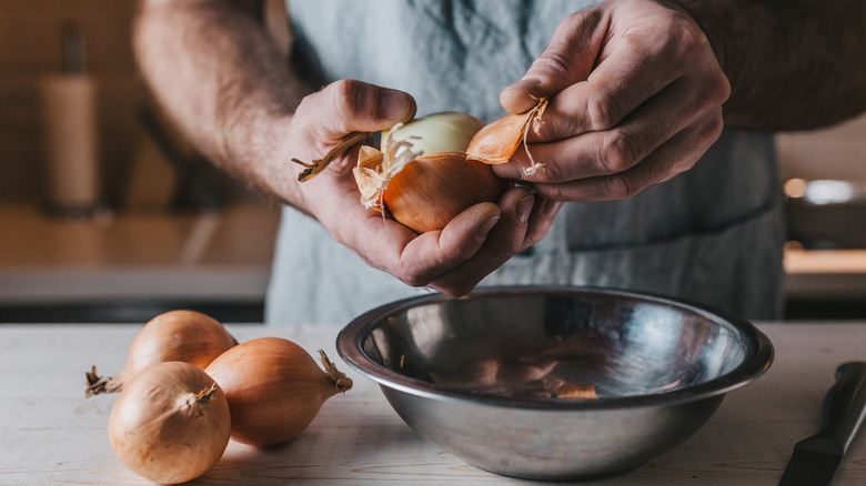 A man's hands shown peeling onion skins into a bowl