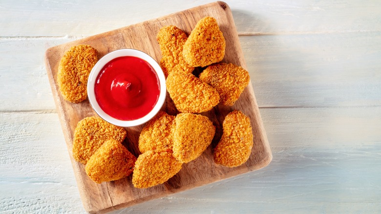 a platter of chicken nuggets sit on a wooden board with a side of ketchup