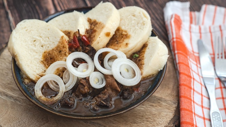 Bread dumplings in a bowl of goulash topped by white onion